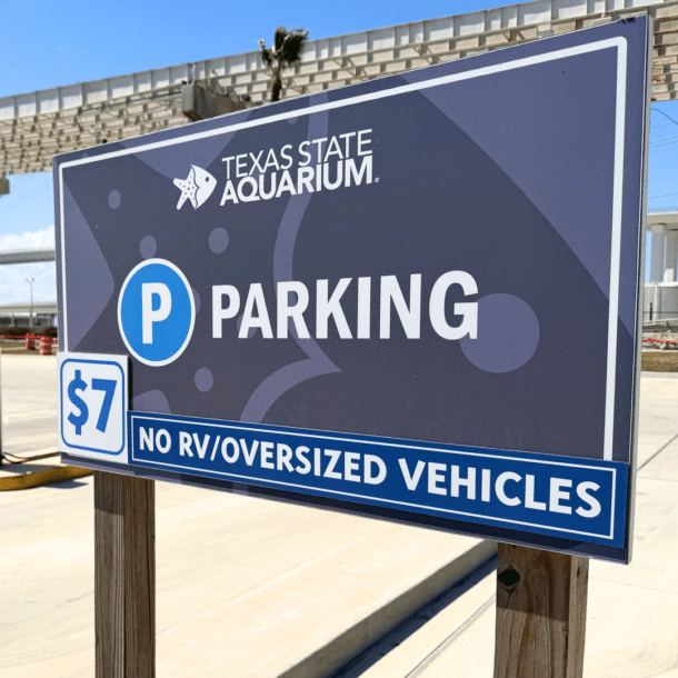 A sign at the Texas State Aquarium parking lot shows a $7 fee and states No RV/Oversized Vehicles with clear blue skies in the background.